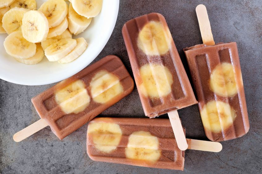 59407688 - chocolate banana popsicles in a cluster with sliced bananas on rustic grey background
