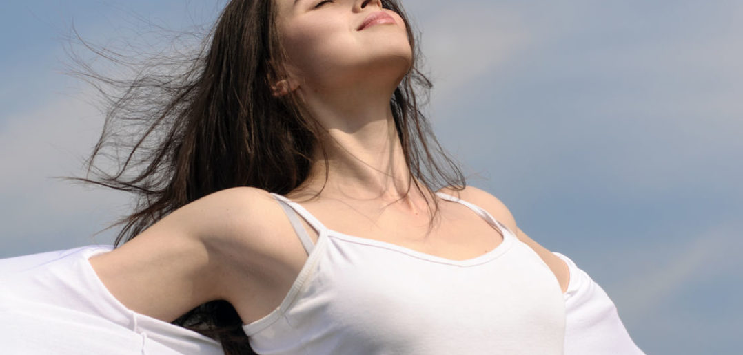 56787526 - girl breathes in fresh air on a blue sky background. she stands her arms to the side and her hair fluttering in the wind. she is wearing in a white loose-fitting clothing. concept: freedom, health, cleanliness.